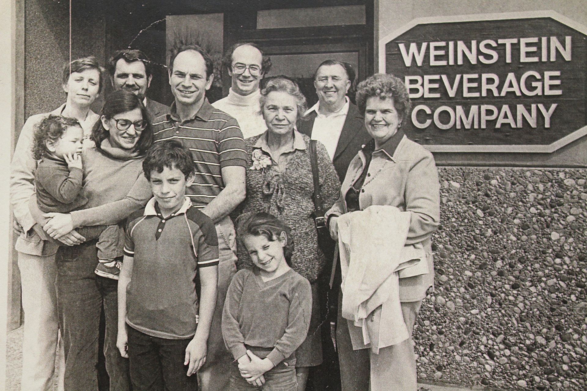 Black and white image of Weinstein Family standing together and smiling outside of the first company building.