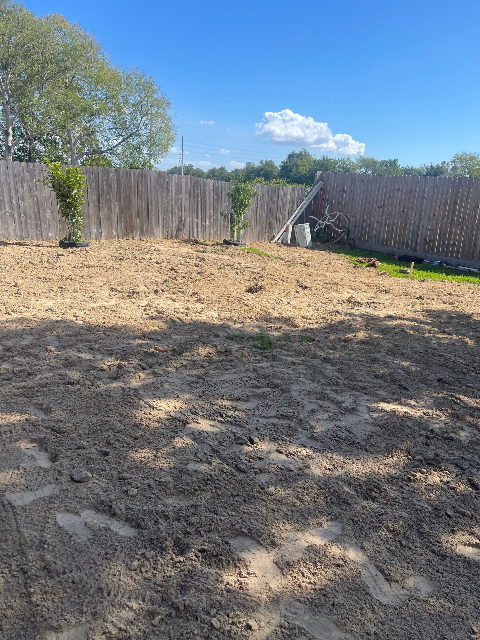 Backyard with brown soil, wooden fence, and blue sky.