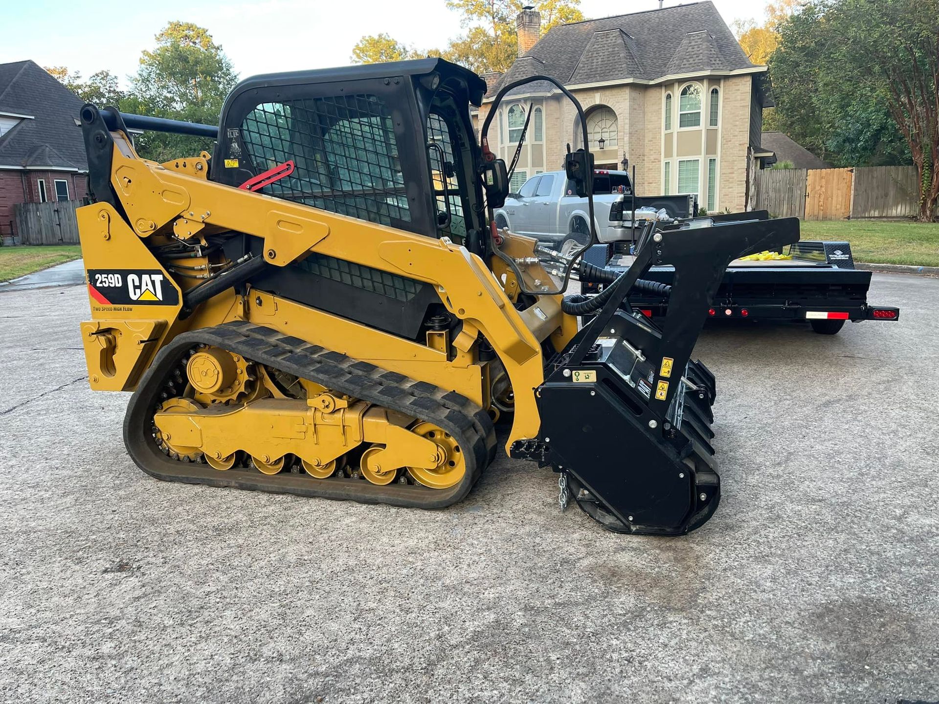 Yellow Caterpillar compact track loader with brush cutter attachment parked on concrete.