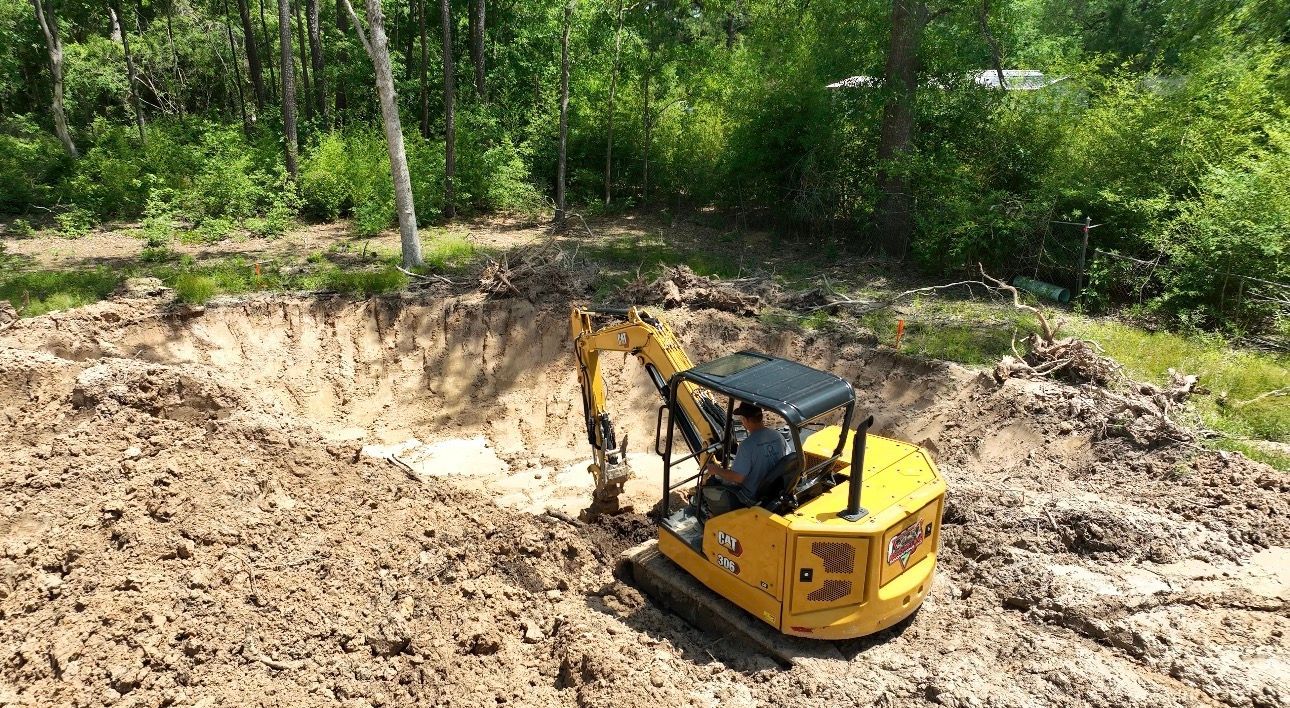 Pond in a grassy field under a cloudy sky. Tall grasses surround the water. Distant trees and buildings.