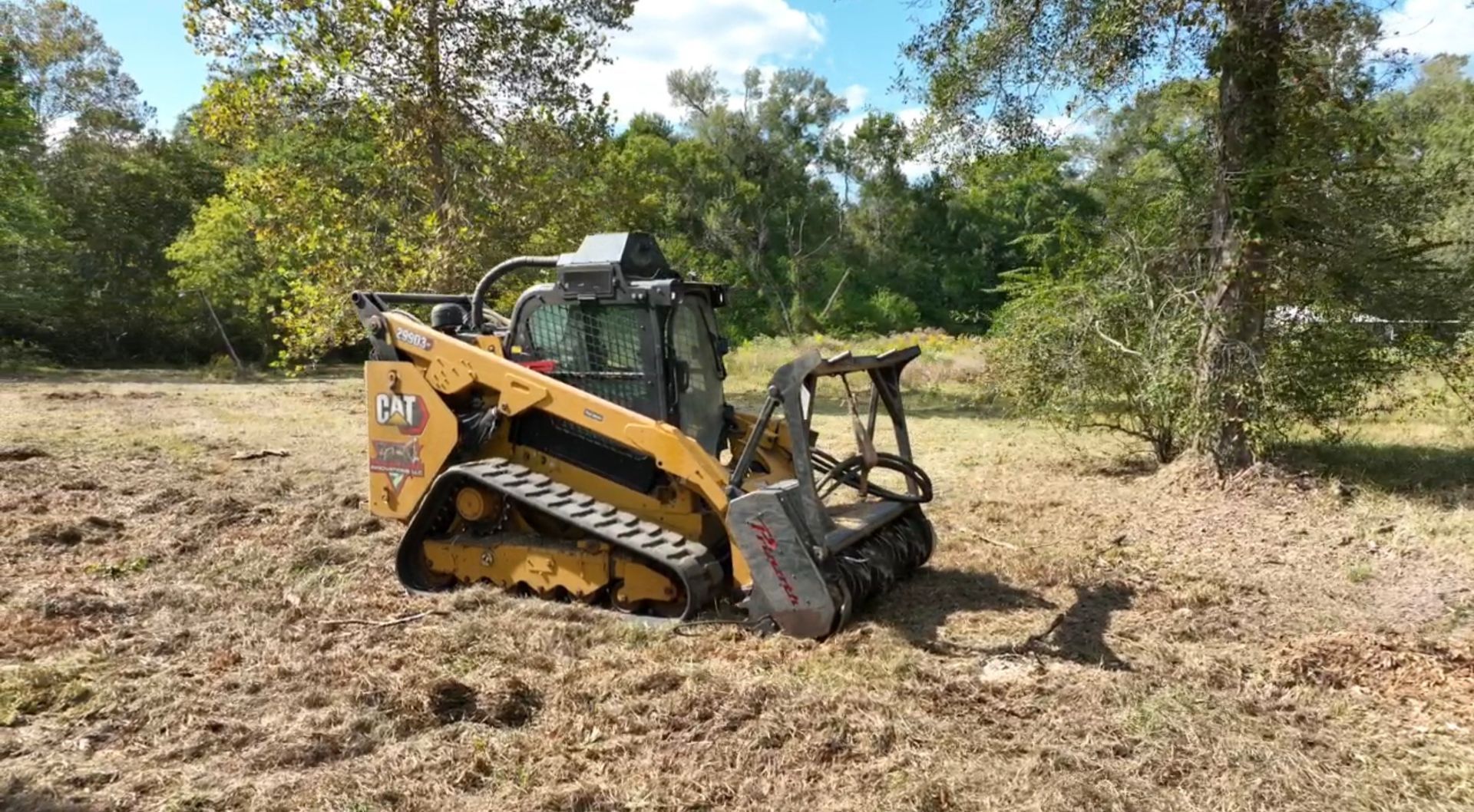 Yellow and black tracked skid steer with forestry mulcher clears a wooded area.