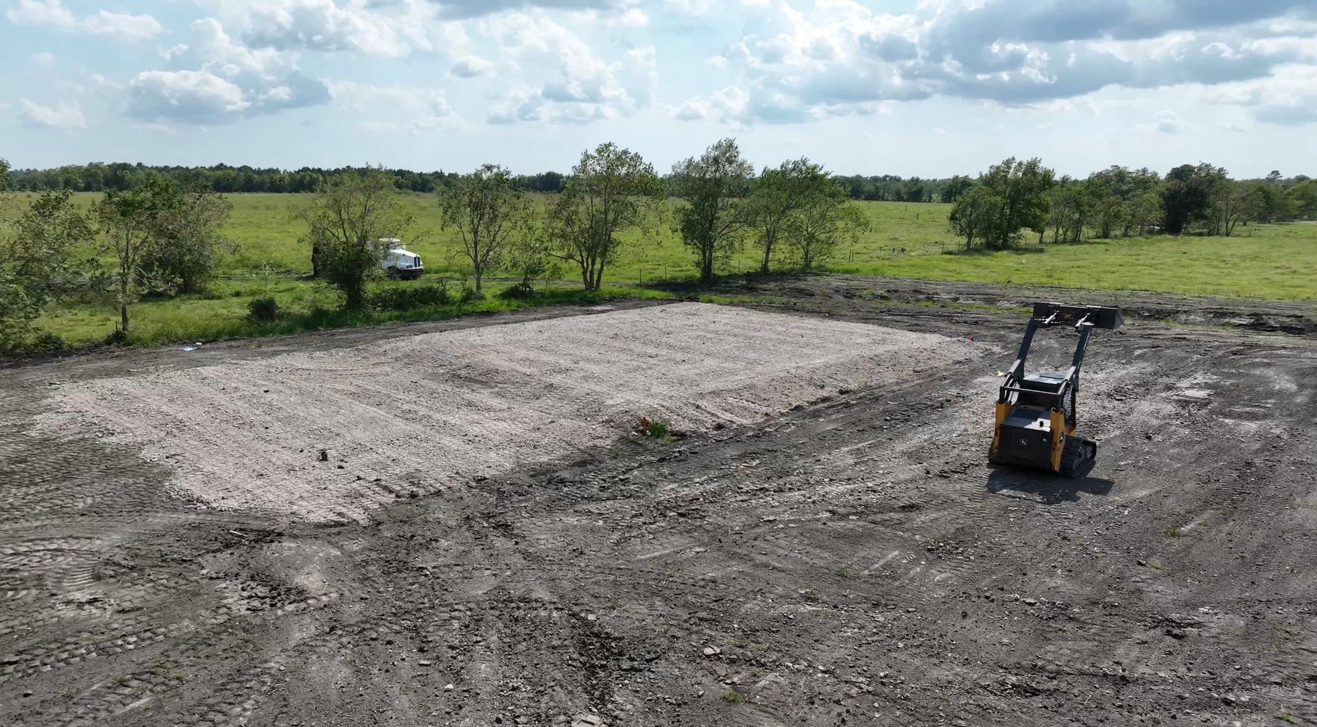 Cleared lot next to a stucco building, with trees in background, sunny day.