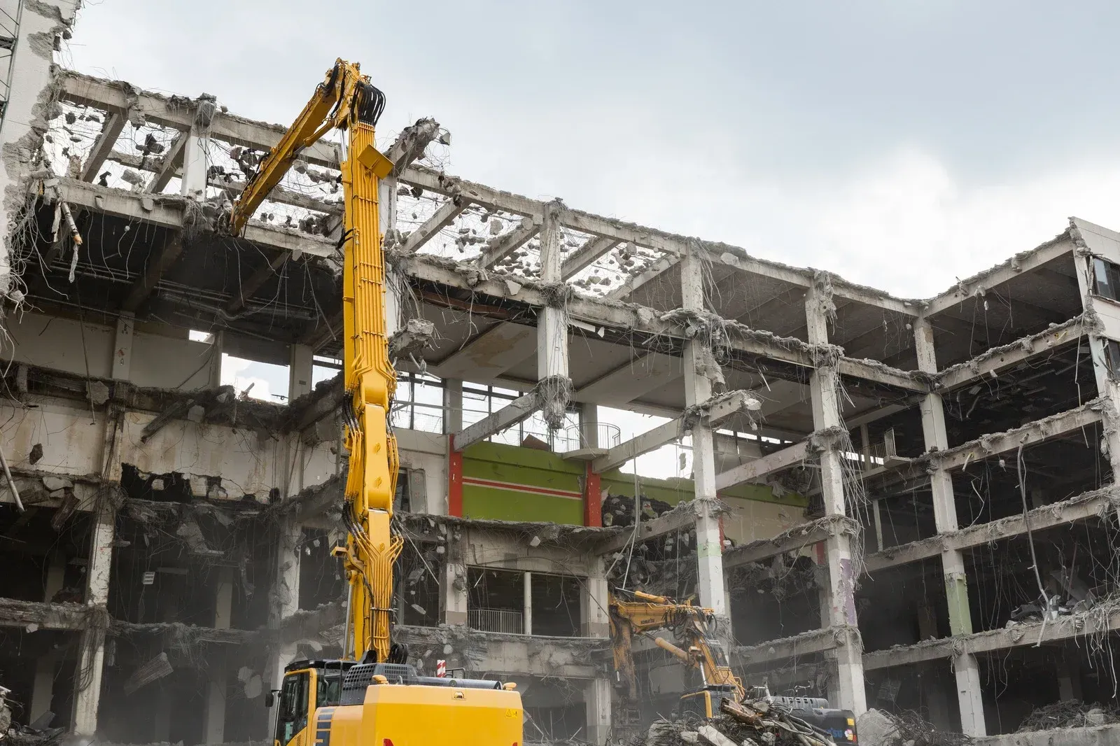 Yellow excavator demolishing a multi-story building. Debris and dust fill the air.