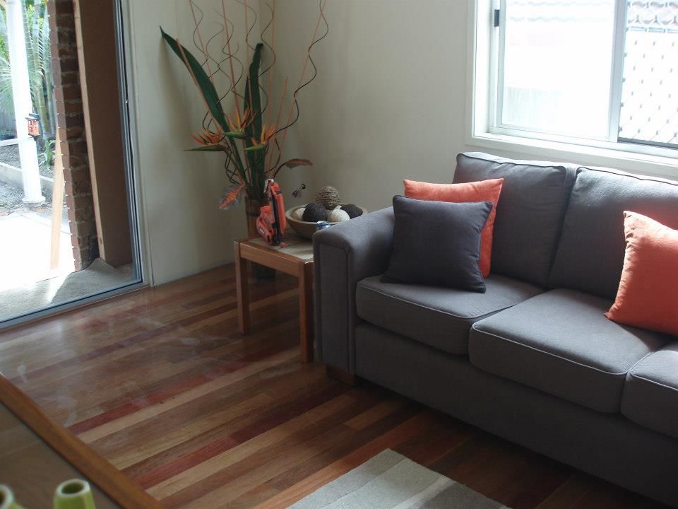 A Living Room With a Grey Couch and Orange Pillows — Timberfection Queensland in Yatala, QLD