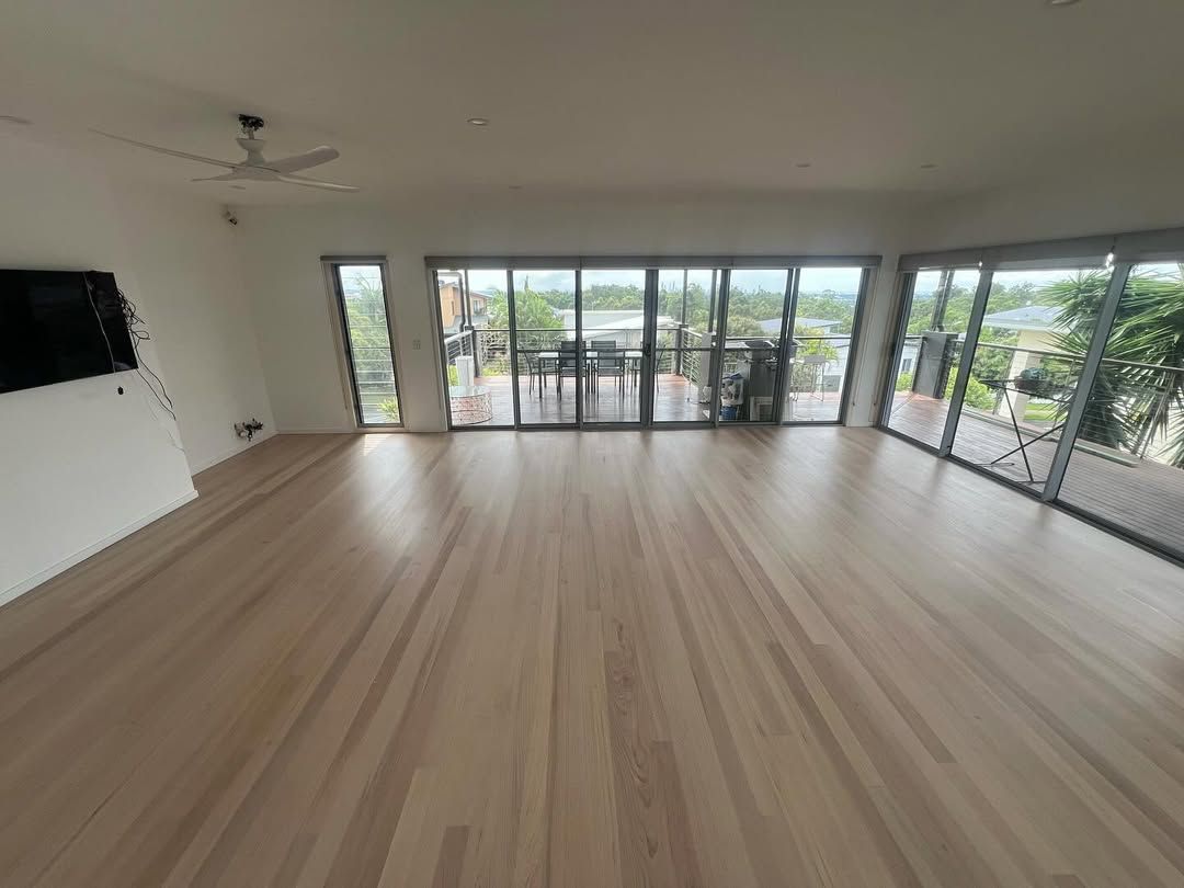 A Large Living Room With Hardwood Floors and Lots of Windows — Timberfection Queensland in Yatala, QLD
