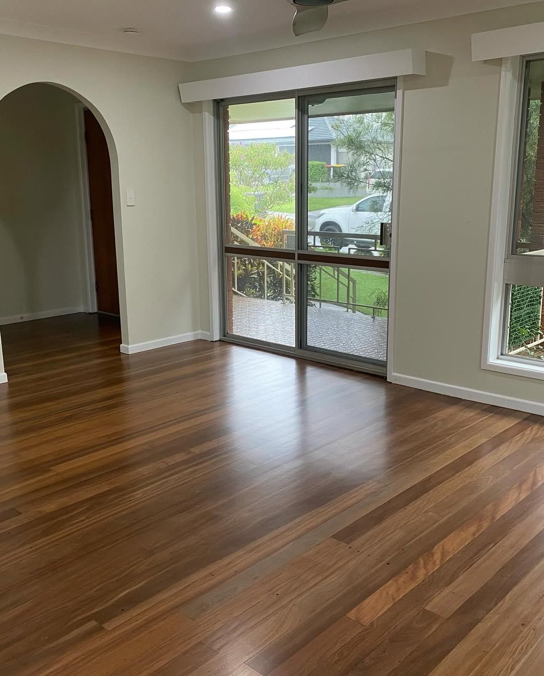 An Empty Living Room With Hardwood Floors and Sliding Glass Doors — Timberfection Queensland in Yatala, QLD