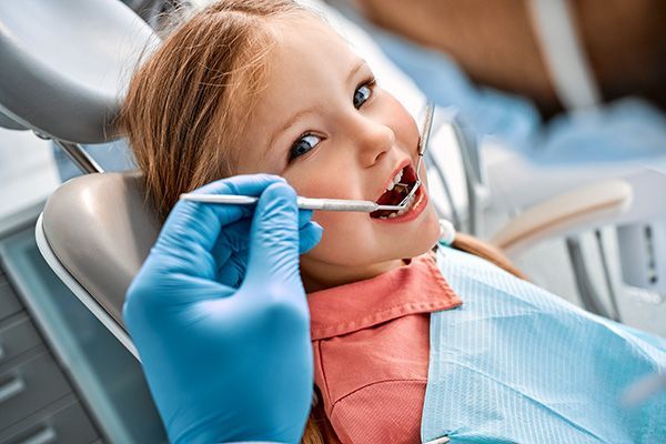 een klein meisje zit in een tandartsstoel en laat haar tanden onderzoeken door een tandarts.