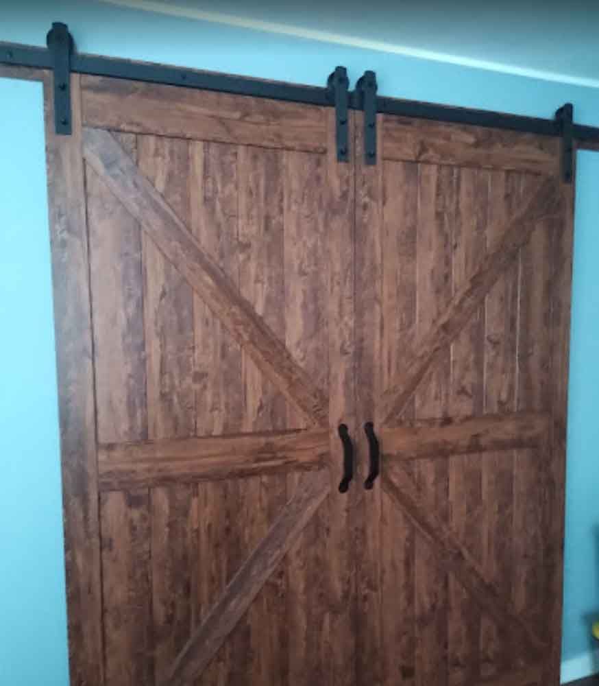 A pair of wooden sliding barn doors with black handles in a room.