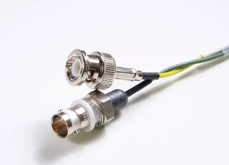 Two BNC connectors with attached cables, one silver-toned and one with a black sleeve, on a white background.