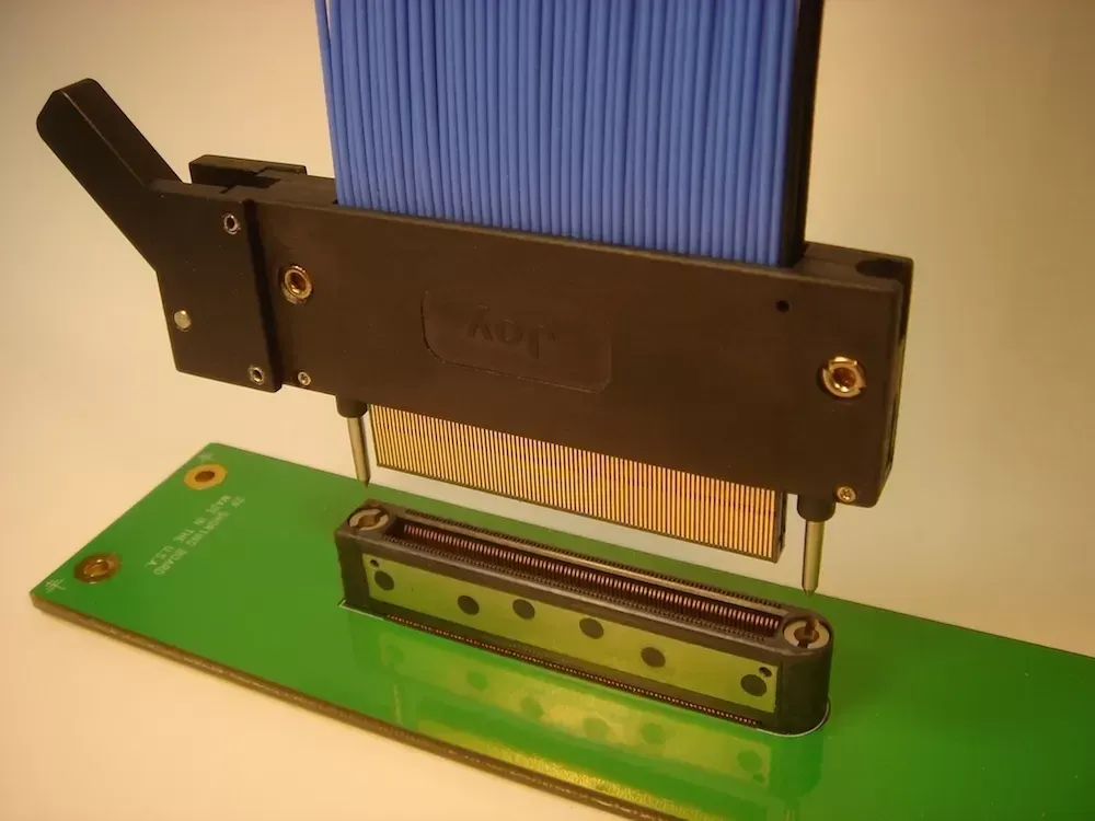 A blue ribbon cable connector aligned above a corresponding socket on a green printed circuit board.