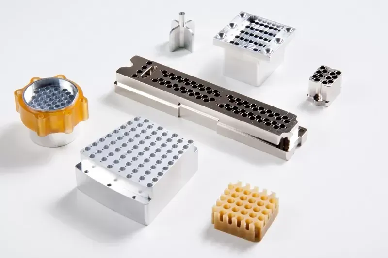 Various precision-machined industrial components, including multi-pin connectors and grid blocks, on a white background.