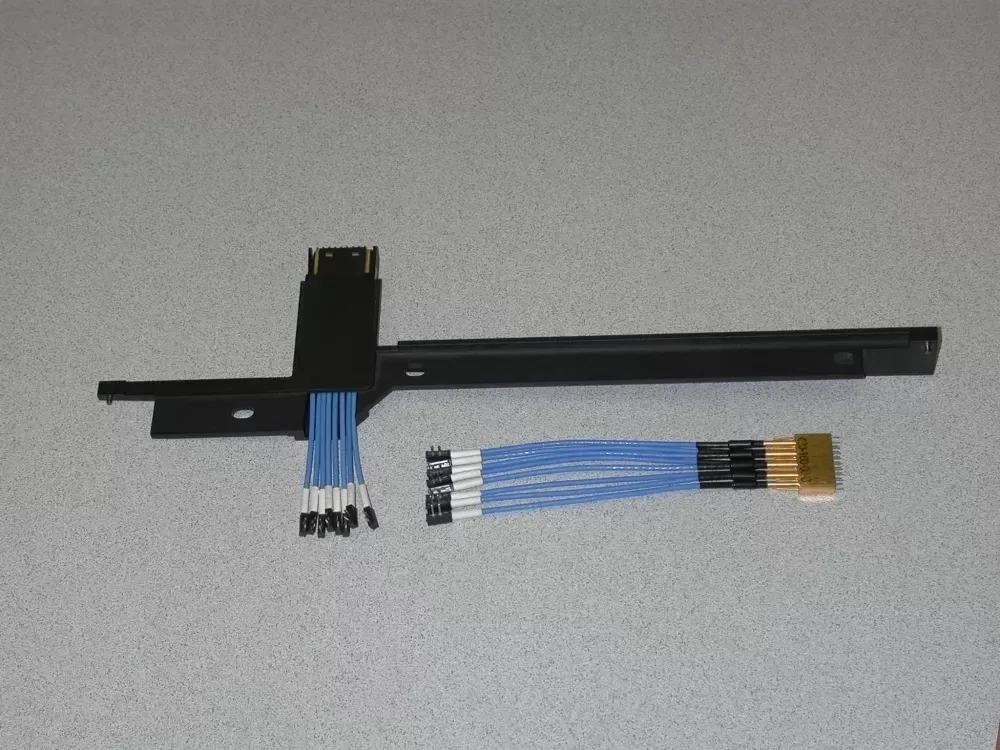 A black metal bracket with a wiring harness and a separate blue wire cable with connectors lying on a gray surface.