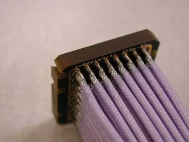 A close-up of a dark connector block with multiple lavender-colored wires soldered to its metallic pins.
