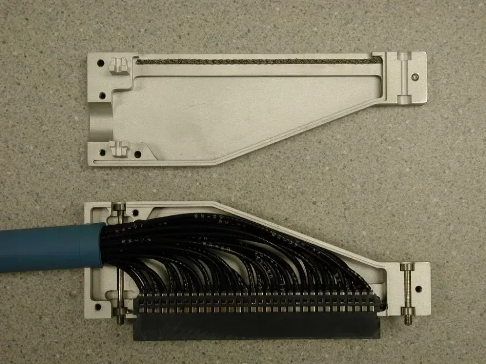 A disassembled D-sub connector shell with a multi-wire cable connected to the pin block, shown against a gray surface.