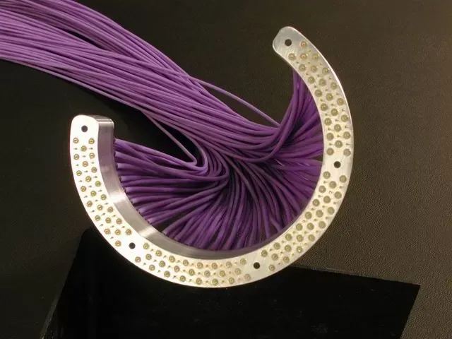 A metallic, crescent-shaped device with many holes holds a dense bundle of purple fiber optic cables.