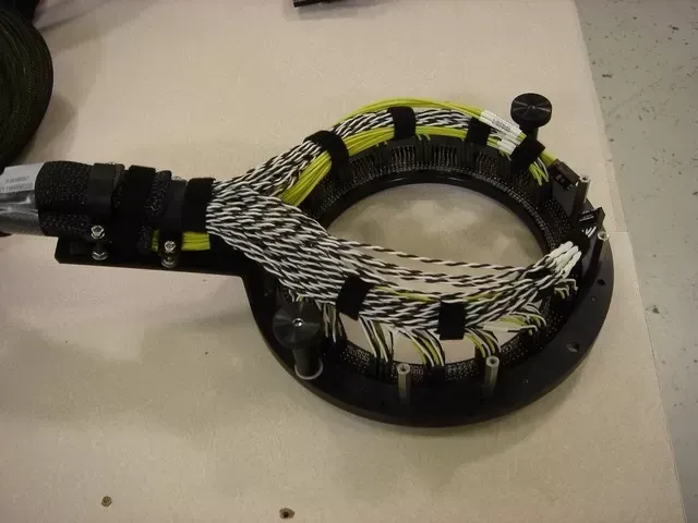 A round mounting ring with numerous black-and-white braided wire bundles secured by black velcro straps.