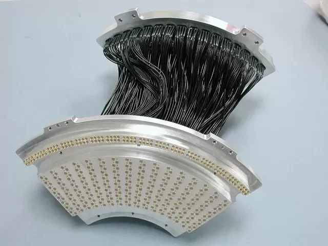 A curved, metallic component with a grid of golden connectors connected by a dense bundle of black wiring.