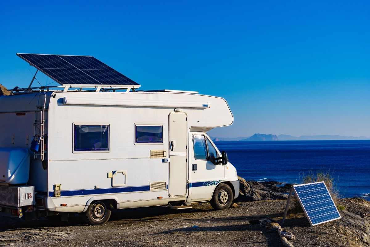 a rv with a solar panel on the roof is parked next to the ocean