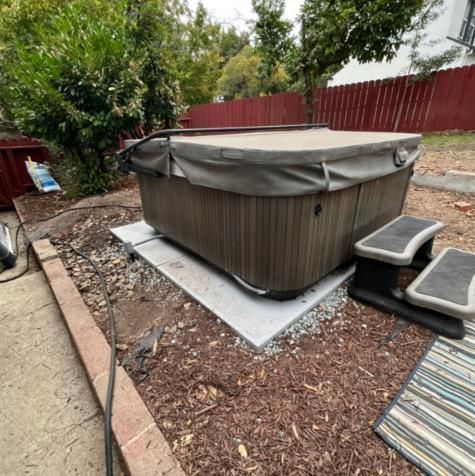 A hot tub is sitting on top of a concrete platform in a backyard.