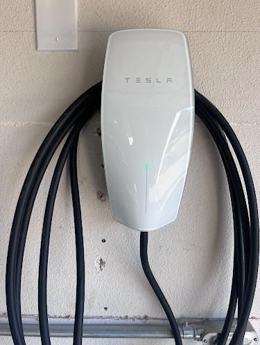 A white tesla charging station is attached to a wall with black wires.