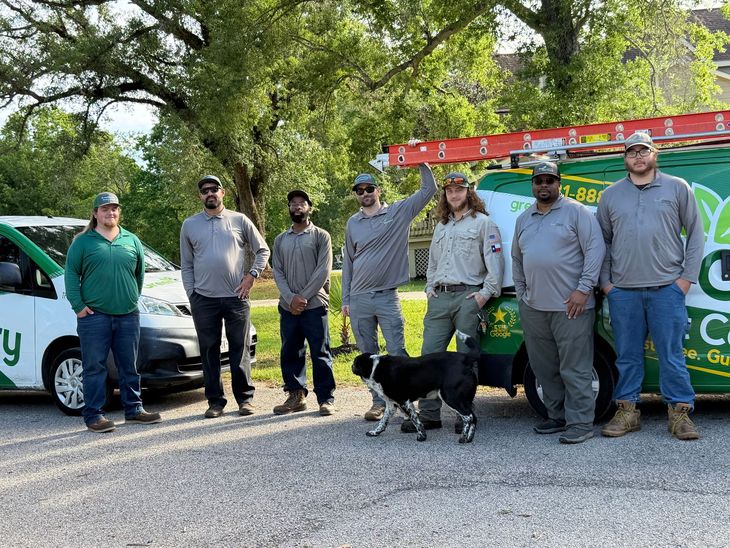 Group of people standing outdoors, near vehicles. Many wearing dark shirts with a logo.