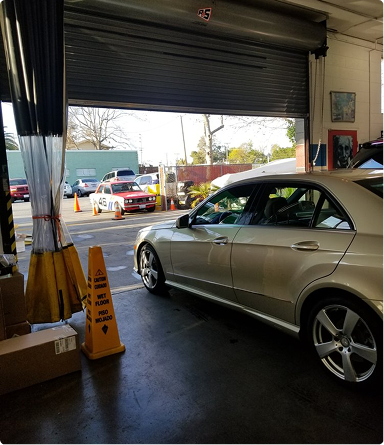 Silver sedan inside a garage with a partially open roll-up door, looking out to a street scene. | Hudson Automotive