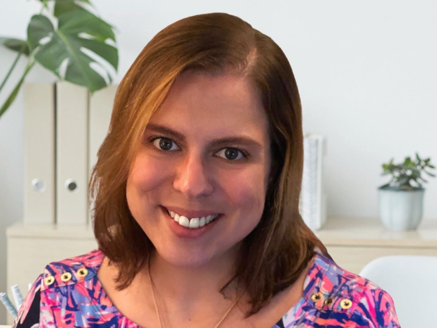A woman in a pink and purple shirt is smiling for the camera.
