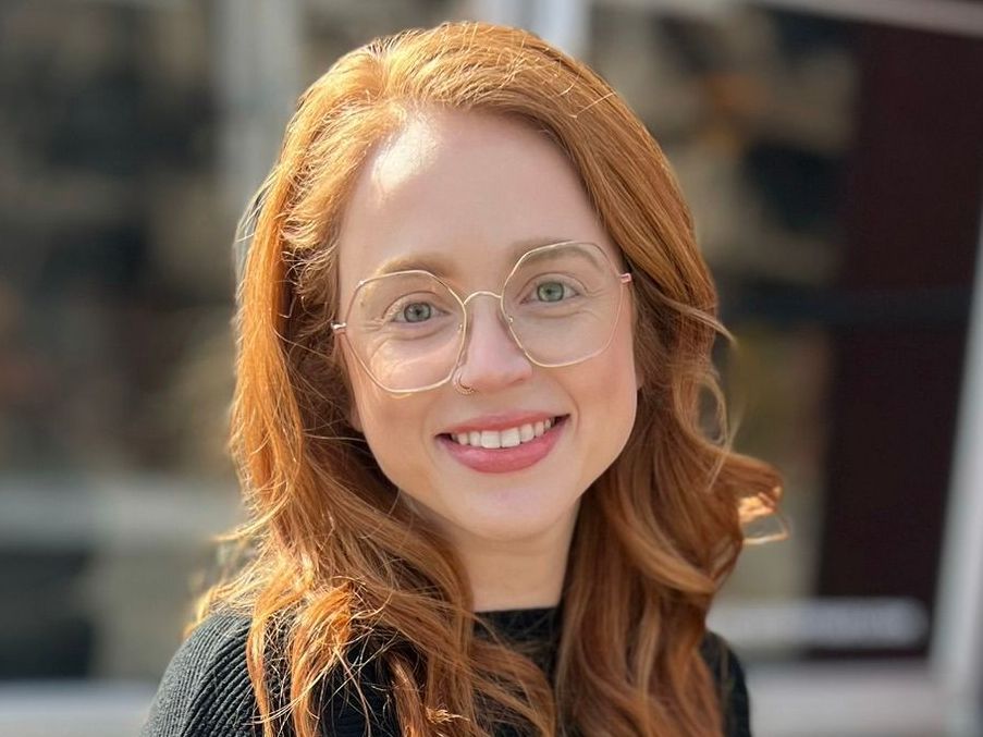 A woman with red hair and glasses is smiling for the camera.
