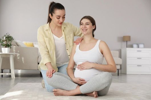 Two pregnant women are sitting on the floor in a living room.