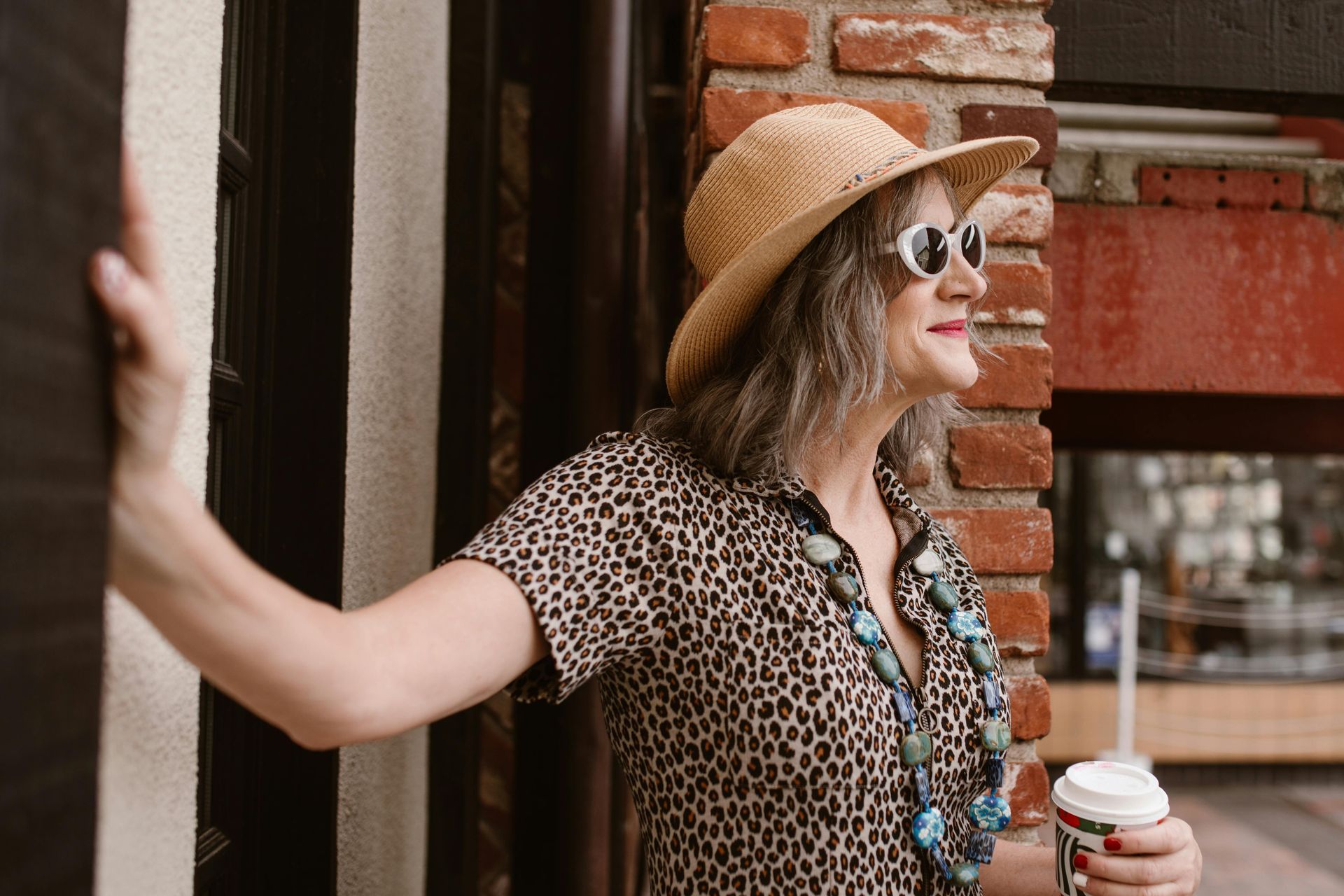 A woman wearing a hat and sunglasses is holding a cup of coffee.