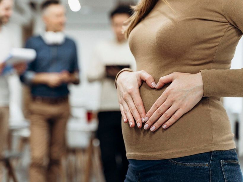 A pregnant woman is making a heart shape with her hands on her belly.