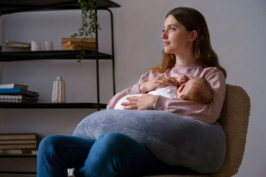 A woman is sitting in a chair holding a baby while breastfeeding.