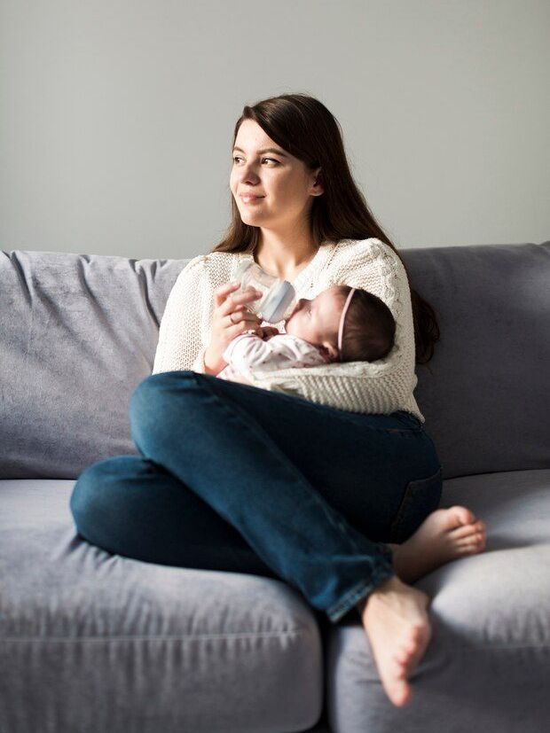 A woman is sitting on a couch holding a baby.
