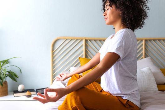 A woman is sitting on a bed meditating with her eyes closed.