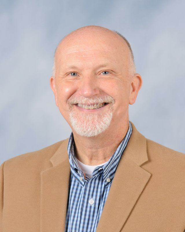 a bald man with a beard is wearing a tan jacket and a blue and white plaid shirt .