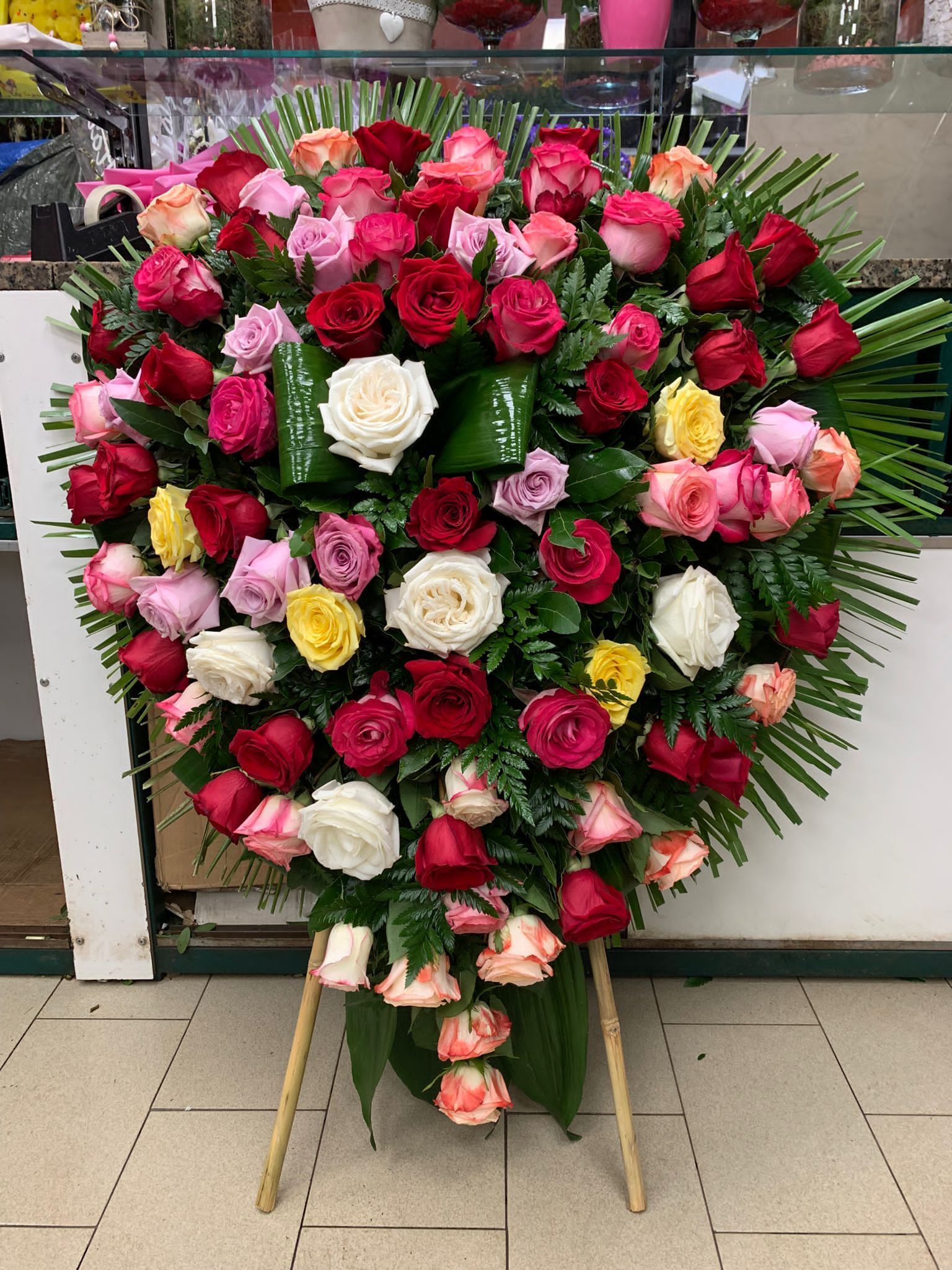 Ghirlanda a forma di cuore composta da rose rosse, rosa e bianche su un cavalletto all'aperto.