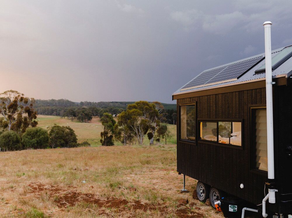 Tiny Black House With Solar Panels on a Grassy Field — Clearspan Builders In Yass, NSW