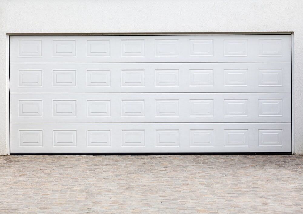 White Garage Door With a Paneled Design in a White Wall; Set on a Brick Paved Ground — Clearspan Builders In Michelago, NSW