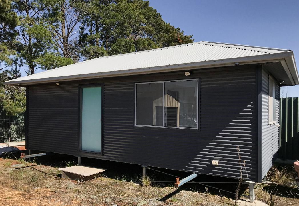 A Small Black House with A White Roof Is Sitting on Top of A Dirt Hill — Clearspan Builders In Queanbeyan East, NSW