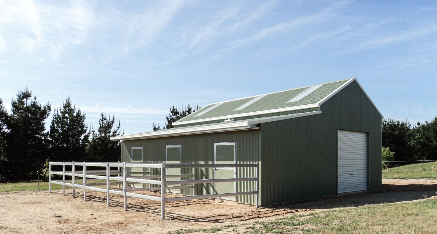 A Green Barn with A White Fence Around It — Clearspan Builders In Queanbeyan East, NSW