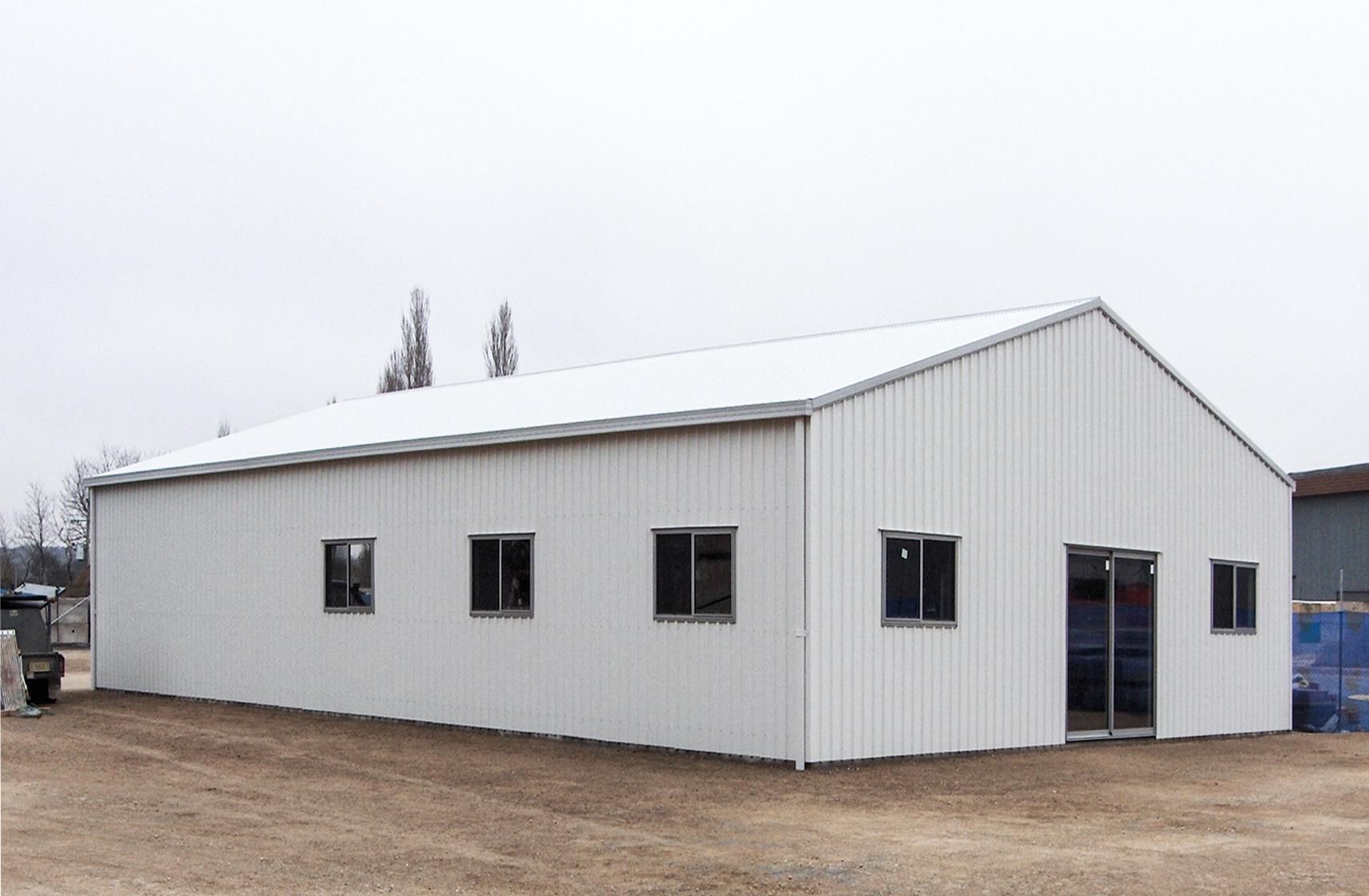 A Large White Building with A White Roof and Windows Is Sitting in A Dirt Field — Clearspan Builders In Queanbeyan East, NSW