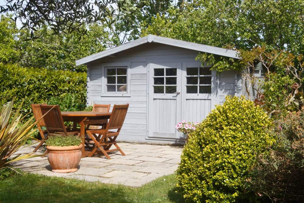 Garden Shed With a Small Table and Chairs on a Stone Patio Surrounded by Greenery — Clearspan Builders In Braidwood, NSW