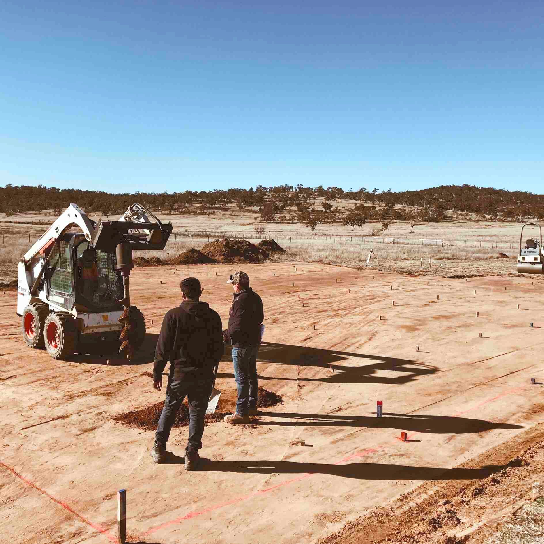 Two Men Standing In A Dirt Field With A Bobcat In The Background — Clearspan Builders In Queanbeyan East, NSW