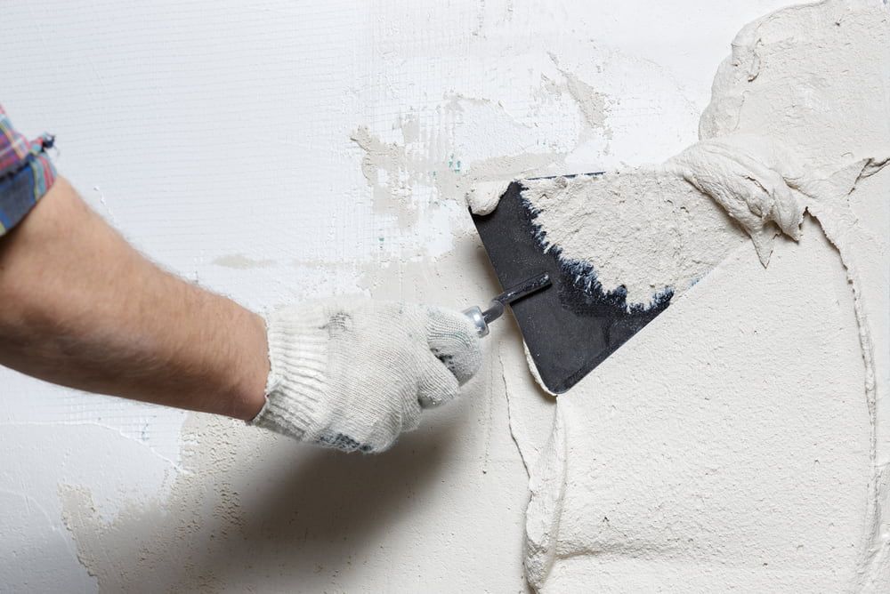 Person in Gloves Uses a Trowel to Apply Plaster to a White Wall — Clearspan Builders In Michelago, NSW