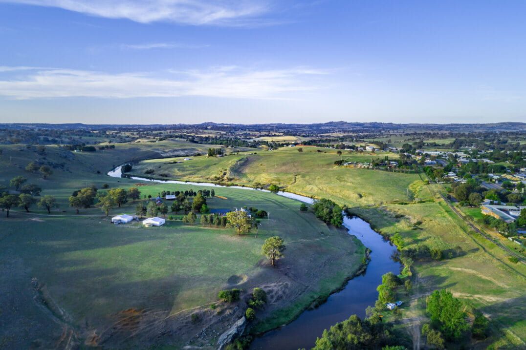 Aerial View of a River Winding Through Green, Grassy Hills Under a Blue Sky — Clearspan Builders In Yass, NSW