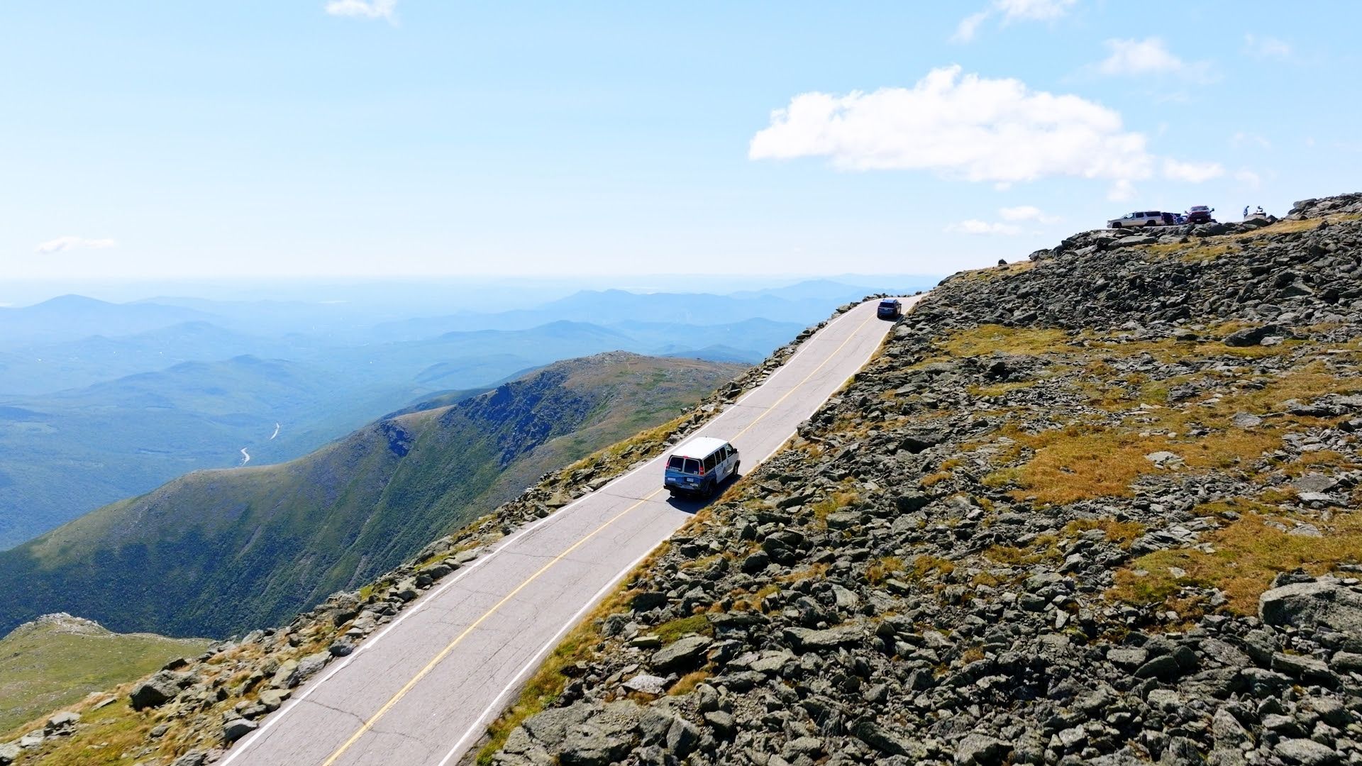 A white van is driving down a mountain road.