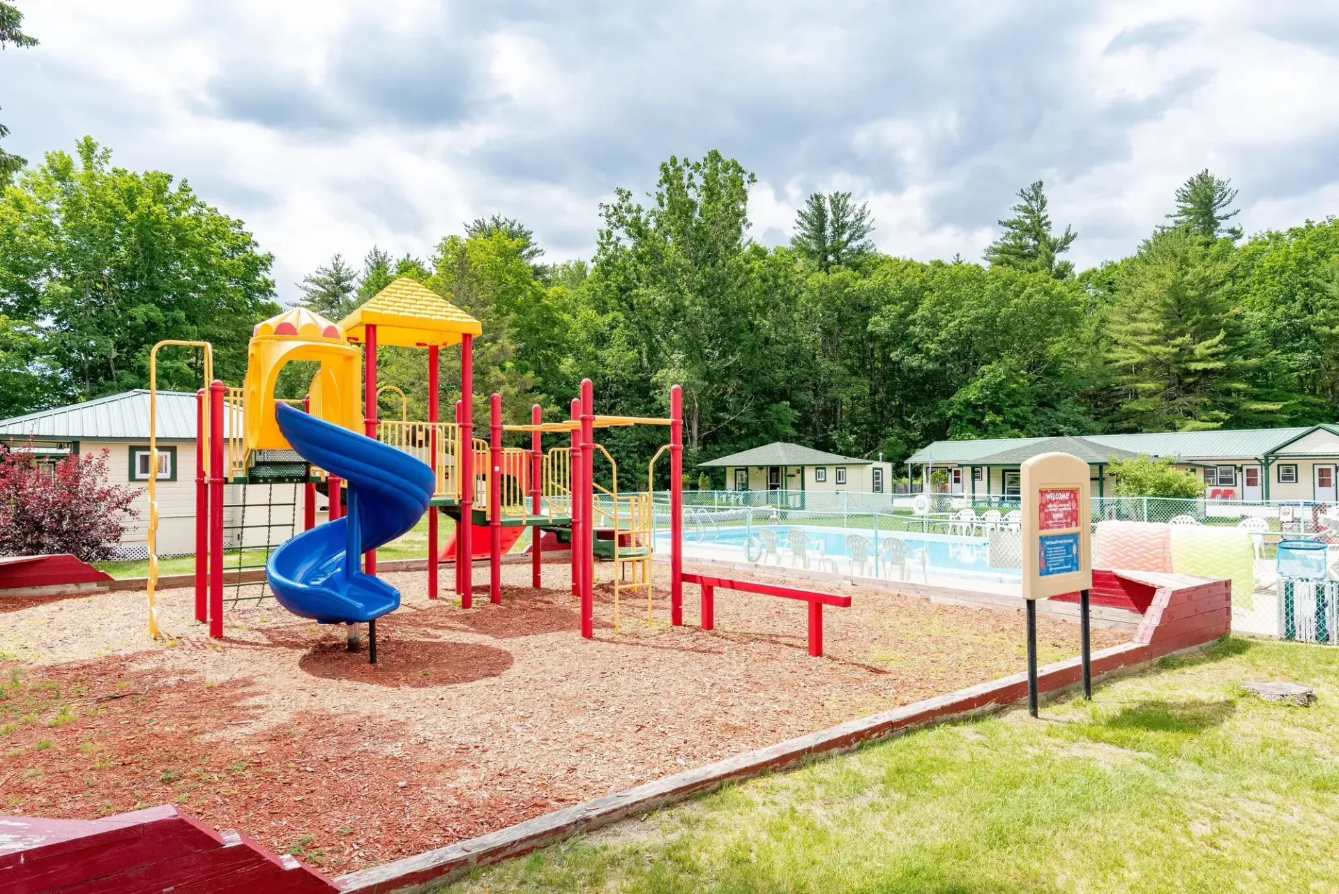 A colorful playground with a slide and a swimming pool in the background.