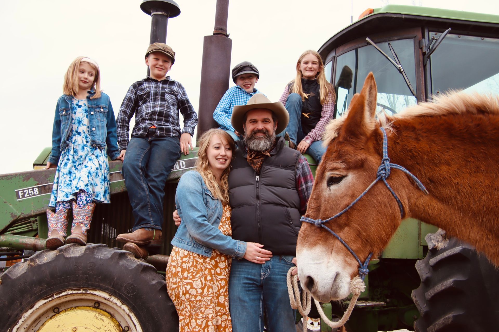 A family is posing for a picture next to a horse on a tractor.