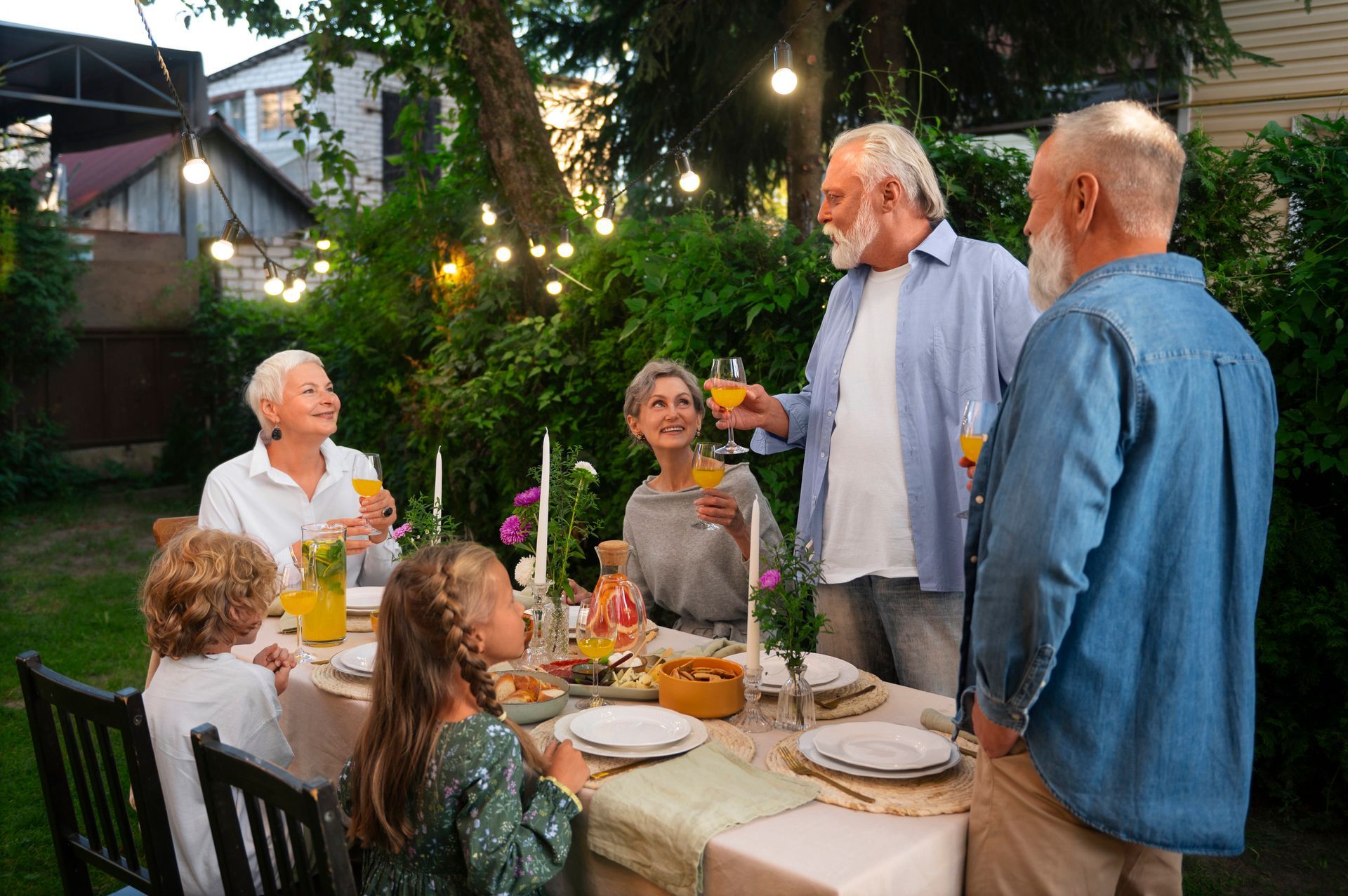 Family toasting at an outdoor dinner table; string lights illuminate the garden.