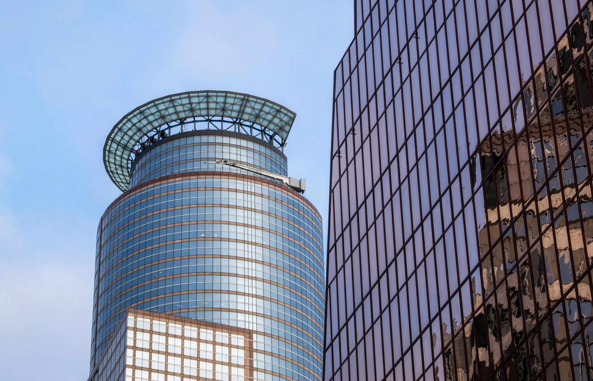 Skyscrapers with glass facades against a blue sky. The cylindrical tower has a green-tinted roof.